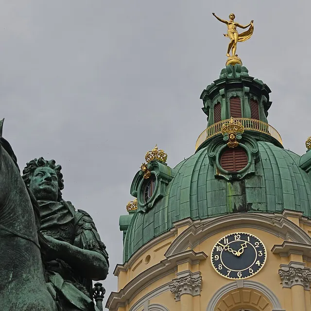 The green copper dome of Charlottenburg Palace crowned by the gilded Fortuna weathervane, with the equestrian statue in front